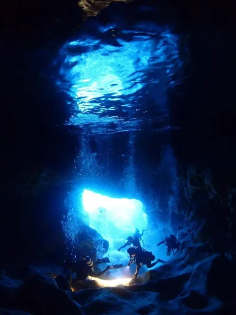 光が差し込む水中の岩場を潜るダイバー