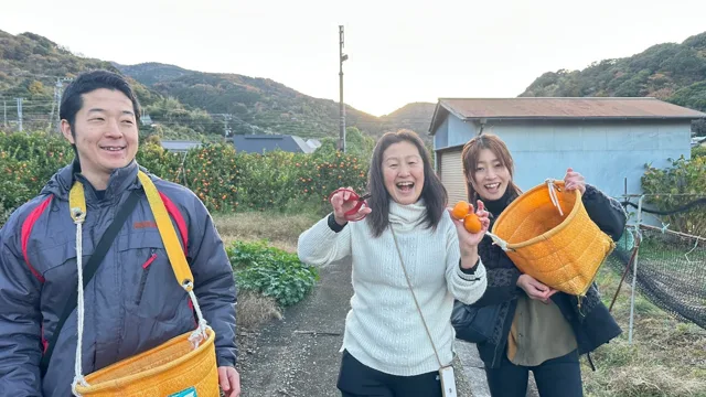 みかんを手に笑顔で記念撮影する3人(ツアー中の観光と推定)