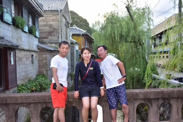 静岡県下田市内（同ツアー写真から推定）での下田市内と見られる街並みの橋で並ぶ3人の参加者（同ツアー写真から推定）