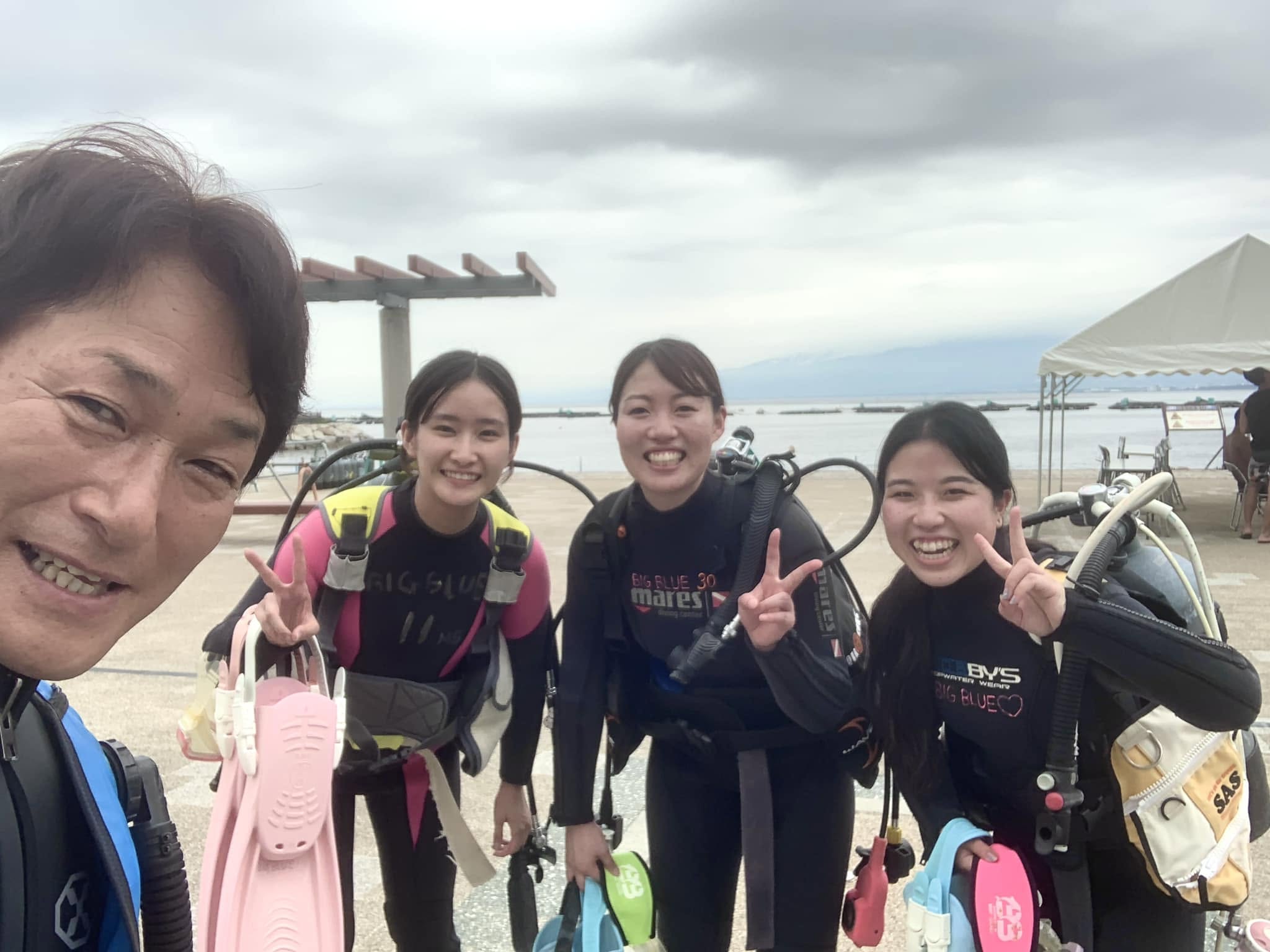 2022年8月5日(投稿日) / ダイビング講習 / 海辺でダイビング器材を着けて講習に参加する3名とインストラクター