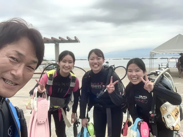 海辺でダイビング器材を着けて講習に参加する3名とインストラクター